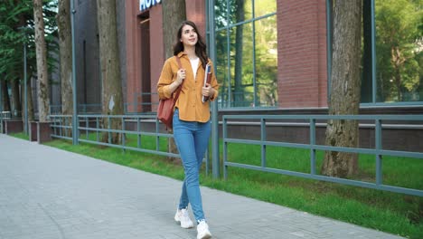 full length view of caucasian student woman while walking down the street near the college