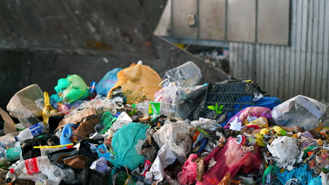 An excavator unloading waste into a large heap of garbage at waste sorting plant. Slow motion