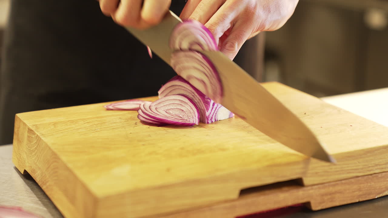 Chef carefully chops an onion with a knife on a wooden board using clean hands, demonstrating precision and hygiene