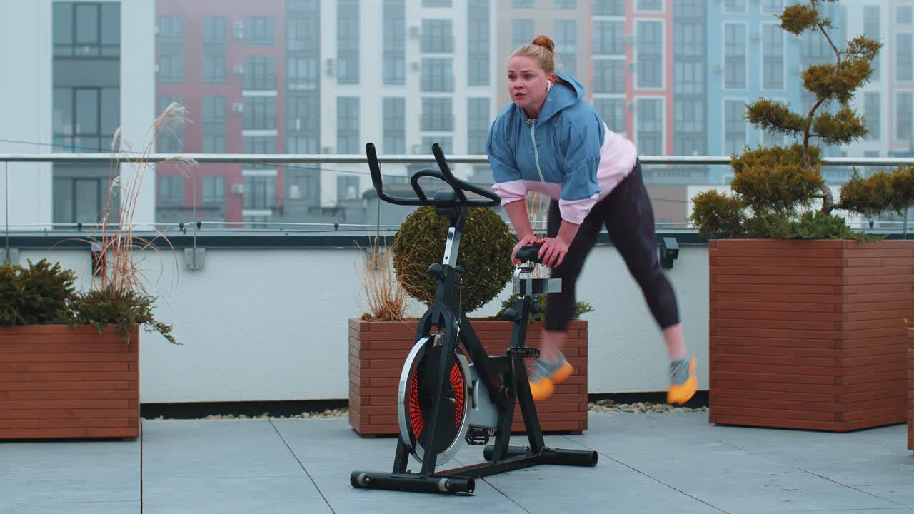 mujer blanca sana haciendo ejercicio en una máquina de ciclismo estacionaria bicicleta en el gimnasio de la azotea de la casa