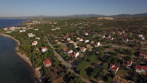 Vista-Aérea-De-Tierras-Verdes-Y-Casas-En-La-Costa-Del-Mar-Playa-Trikorfo-Grecia