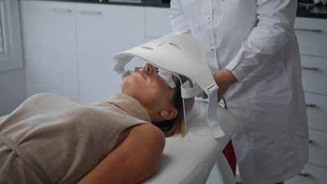 cosmetologist doing skin treatment turning on led mask in beauty clinic close up