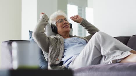 Mujer-Mayor-Afroamericana-Con-Auriculares-Escuchando-Música-Sentada-En-El-Sofá-En-Casa