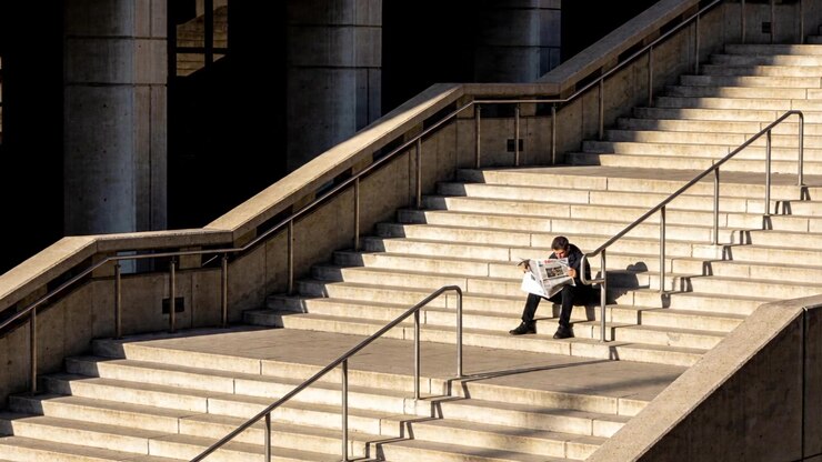 Turning pages man in dark coat on stone steps, resting, reading folded newspaper, bag, copy space