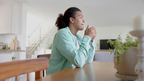 Happy,-thoughtful-biracial-man-with-long-hair-drinking-coffee-sitting-at-dining-table,-slow-motion