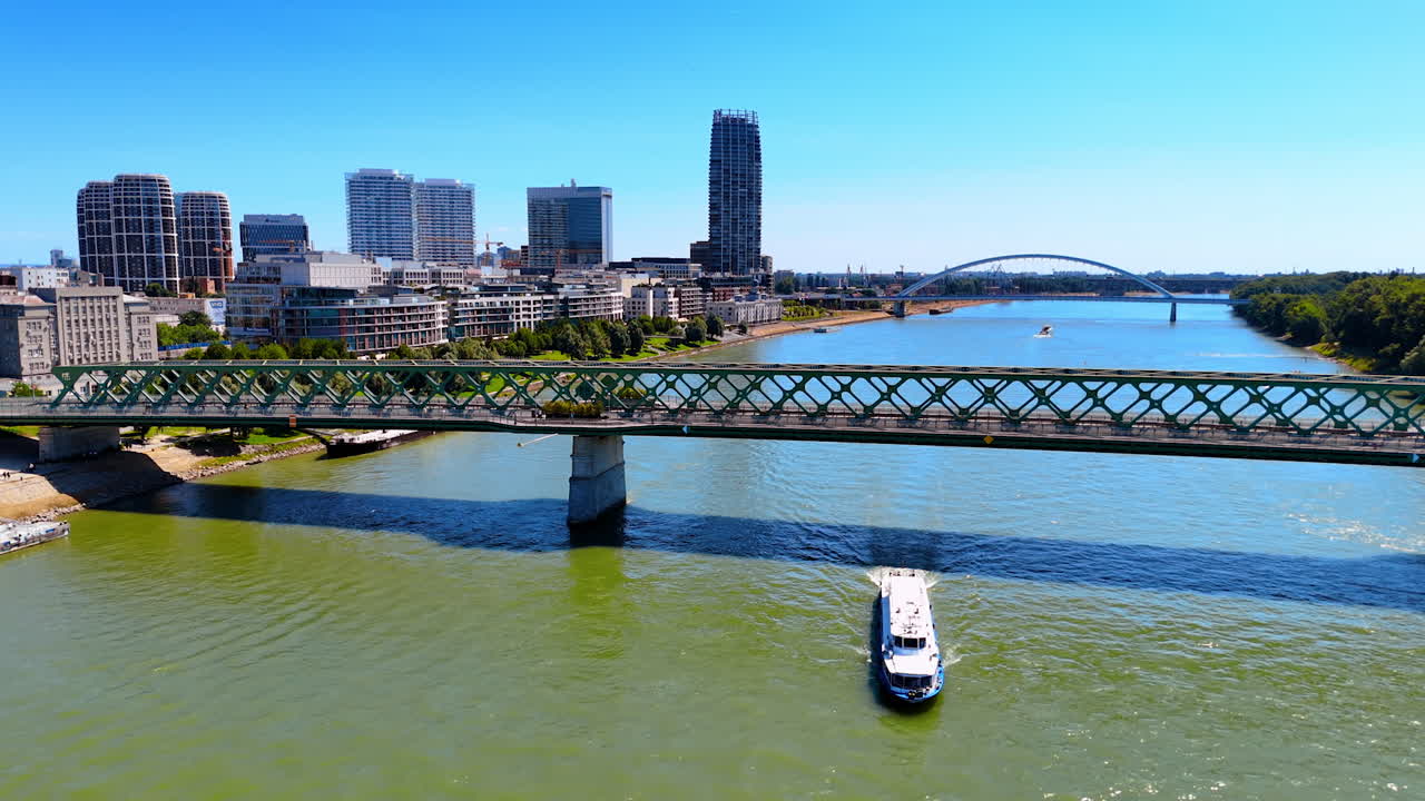 Riverboat floats under the bridge by the Danube River. Modern architecture of Bratislava, Slovakia at backdrop. Aerial view.