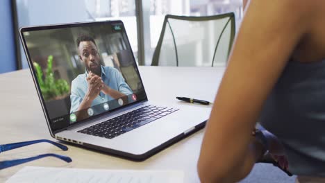 Video-Einer-Gemischtrassigen-Frau,-Die-Auf-Einem-Laptop-Einen-Videoanruf-Mit-Einem-Afroamerikanischen-Männlichen-Kollegen-Führt