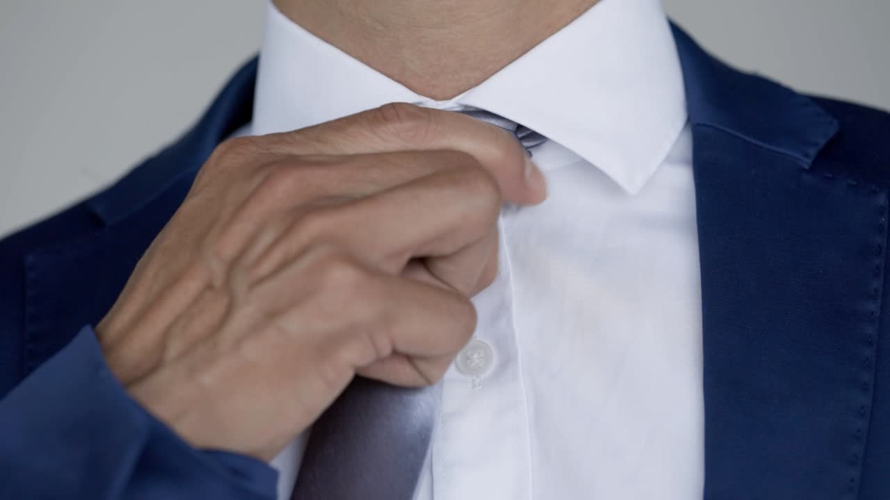 Caucasian male with blue blazer and white shirt adjusts silver tie
