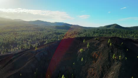 panorámica aérea a través de la montaña de tierra con bosque verde en el fondo, tenerife españa, destello de lente roja