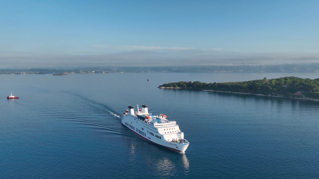 Veduta aerea con drone della nave passeggeri Rigel VII di Ventouris Ferries che naviga nelle calme acque blu del Mar Ionio vicino alla costa dell'isola di Corfù, Grecia