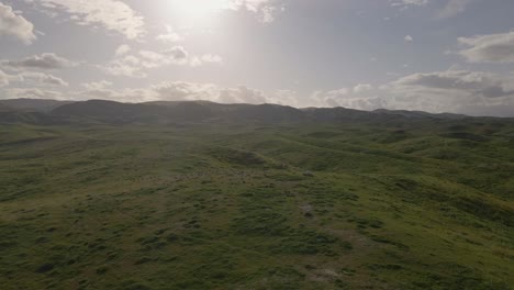 Drone-slowly-pushes-into-vast,-rolling-grassy-fields-ascending-a-mountain-against-a-backdrop-of-a-beautiful-sunset