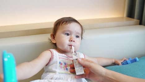 mommy helps cute asian toddler girl to drink juice through a straw while the child is playing