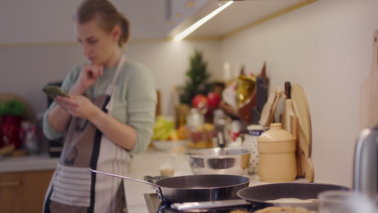 mujer se apoya en un mostrador de la cocina y navega por las redes sociales en su teléfono inteligente