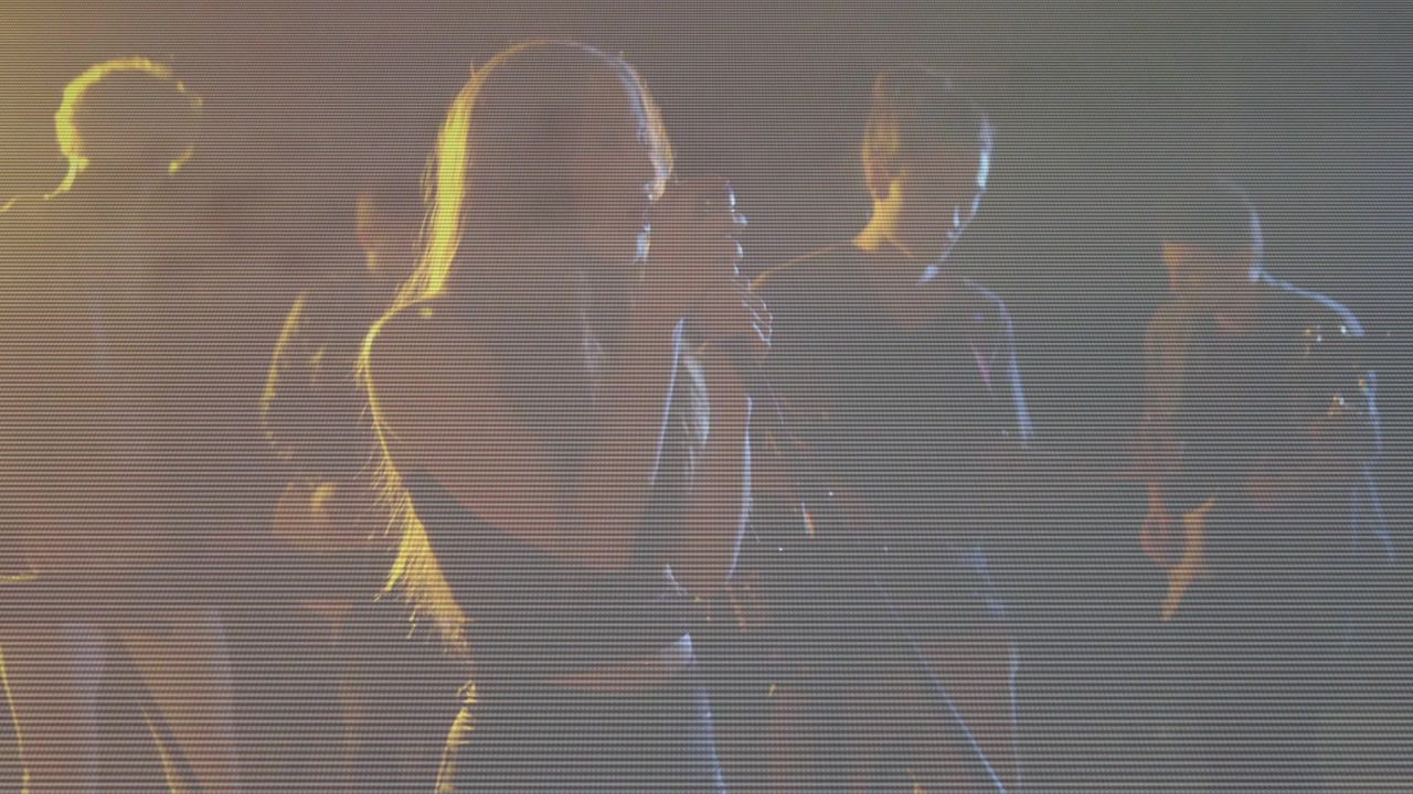 Cámara ascendiendo revelando a una vocalista femenina que avanza, acercando el micrófono y cantando con música emotiva.