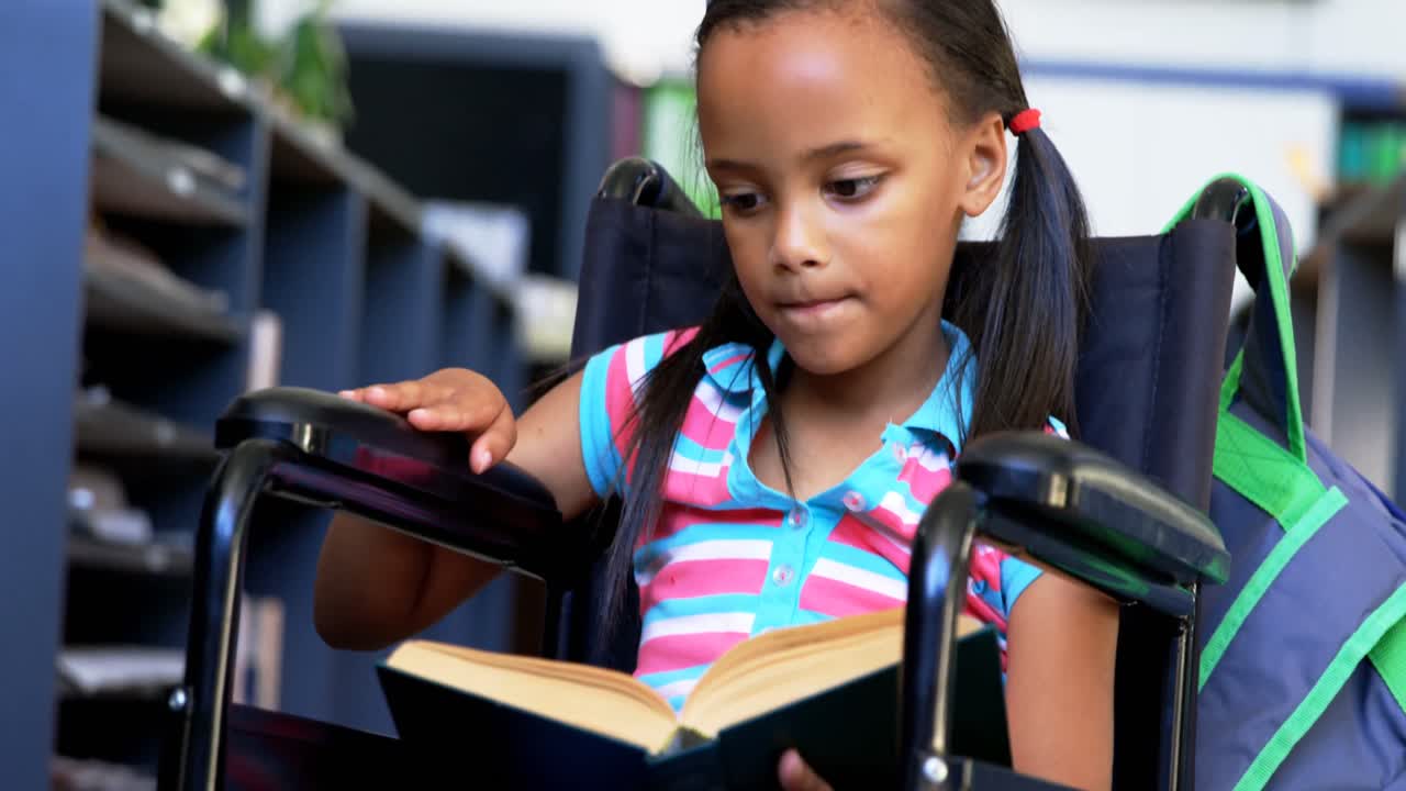 Front view of disabled African American schoolgirl reading a book in library at school 4k