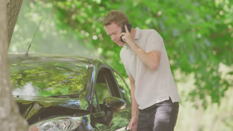 Un-Hombre-Saliendo-De-Un-Auto-Humeante-E-Inspeccionando-Los-Daños-Del-Accidente-Antes-De-Llamar-A-Los-Servicios-De-Emergencia.