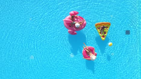 aerial: flying above a group of friends relaxing on floaties during a pool party