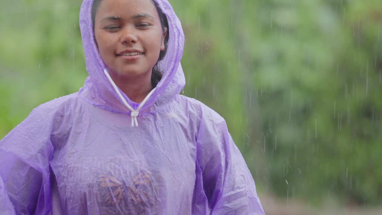 Village girl in waterproof coat enjoying light rain, joyful and carefree mood in rural surroundings, 4k video