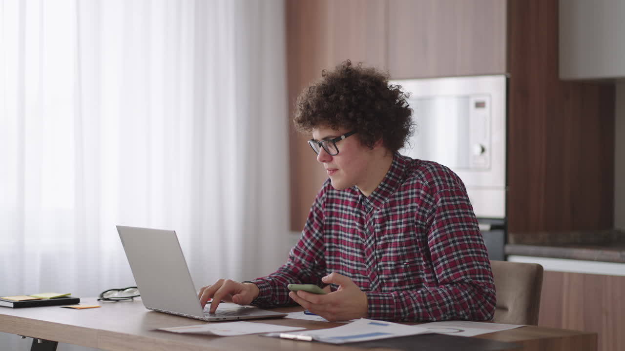 Young man with smartphone in his hands. Modern businessman or student at home office. Freelancer at work. Young student man study at home with laptop and uses a smartphone