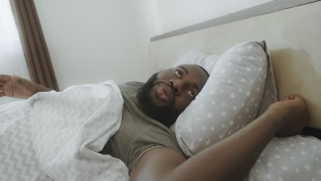 hombre negro escuchando ruido por la mañana. hombre irritado despertando en la cama.