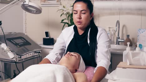 Cosmetóloga-Femenina-Está-Haciendo-Masajes-De-Cuello-En-El-Salón-De-Spa.-Una-Joven-Con-Los-Ojos-Cerrados-Está-Tumbada-En-El-Sofá-Durante-La-Cosmética.