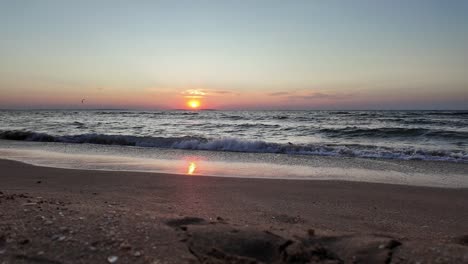 The-sun-sets-beautifully-over-the-Sea-of-Azov,-illuminating-the-sky-with-vibrant-colors-as-waves-gently-wash-onto-the-sandy-shore-of-Crimea