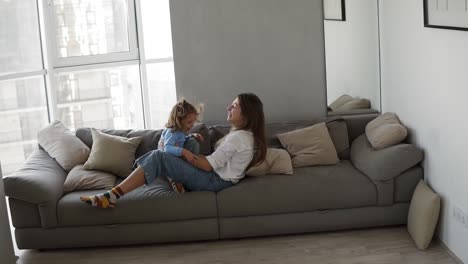 happy family mother and kid daughter having fun together lying on sofa. young woman tickles the girl, raises in outstretched