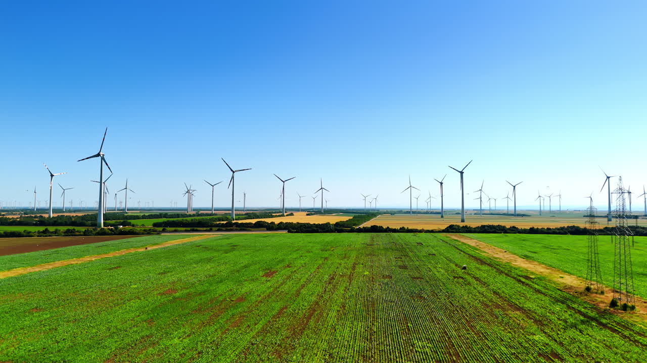 Wind turbines stand over green fields. Wind turbines fill the horizon, creating energy as they rotate above lush green fields on a clear sunny day