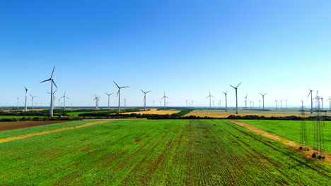 Wind turbines stand over green fields. Wind turbines fill the horizon, creating energy as they rotate above lush green fields on a clear sunny day