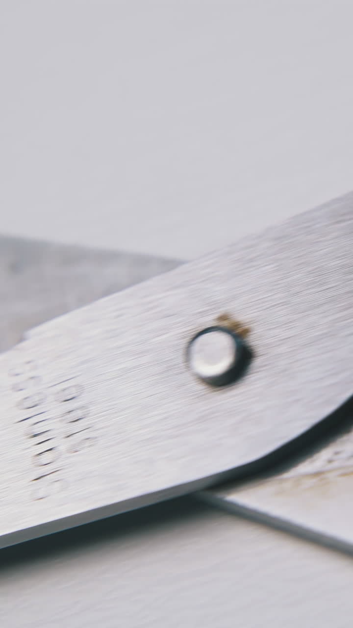motion along open metal scissors with black plastic handles on clean white surface extreme close view