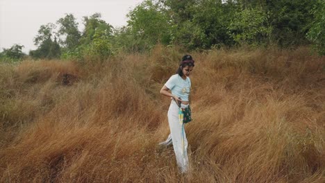 girl tourist with umbrella at rural mountain in bushes bends down and plucks a grass