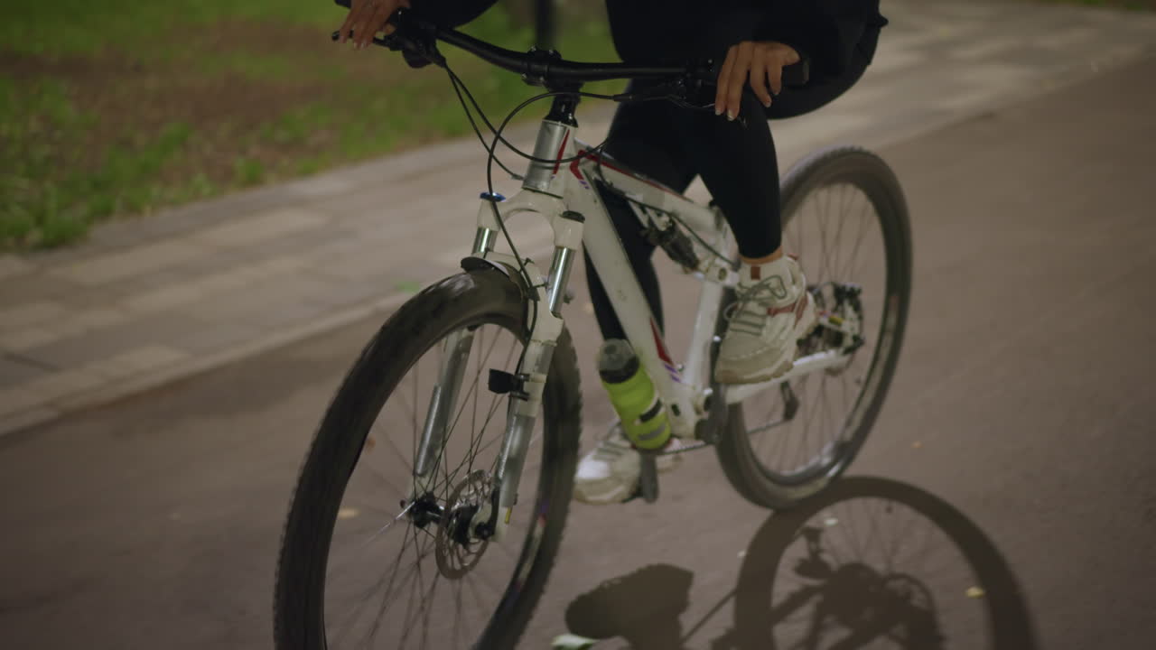 Serene Ride Ongoing, Focused Cyclist Under Gentle Park Illumination, Tranquil Biking Session Beneath Softly Lit Evening Sky, Devoted Rider Maintains Consistent Tempo During Peaceful Nighttime Ride