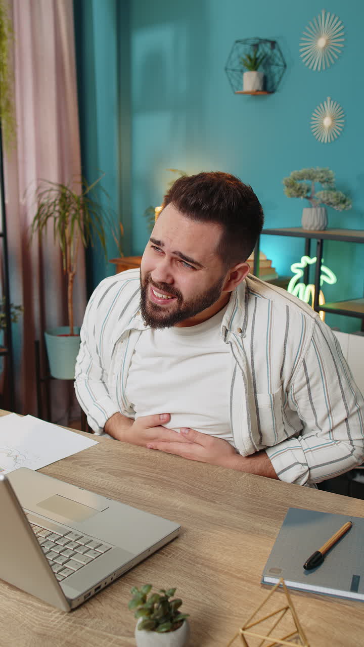 Upset business man feeling stomach ache overeating during work process on laptop in home office