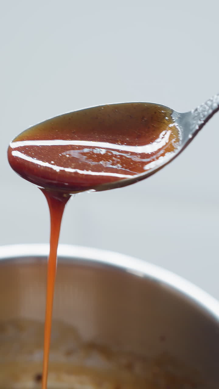 Close-up of golden palm oil being poured from spoon into pot, creating a rich, glossy texture, oil flows smoothly, reflecting warm light, as the pot sits on modern kitchen counter