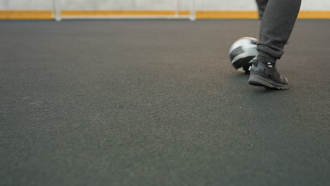 leg view of someone skillfully dribbling soccer ball on sport arena surface during training session, showcasing control and movement precision, background includes fencing and blurred goal area