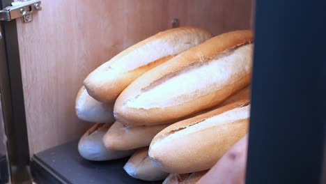 person selecting baguettes from a bakery shelf