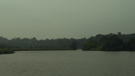 tranquil lake with surrounding greenery under a hazy sky, hinting at early morning serenity or dusk calmness