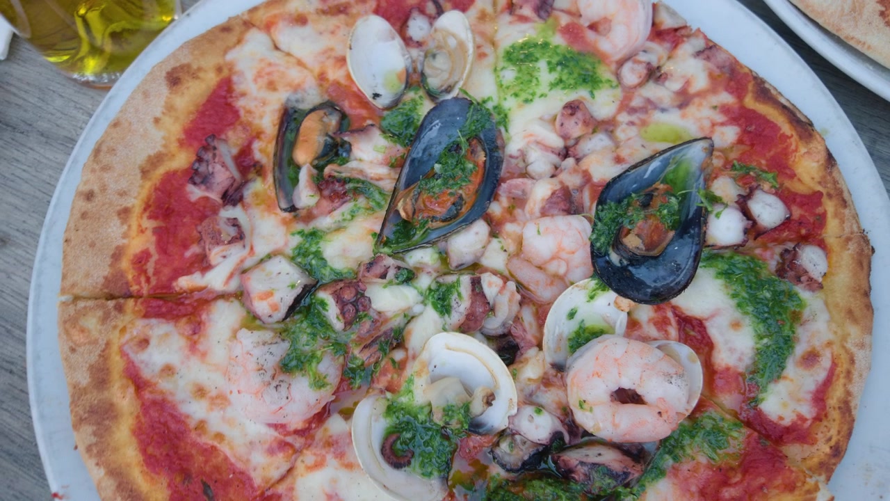Vista dall'alto di una pizza ai frutti di mare con cozze, vongole, gamberi e polpo su un tavolo di legno.