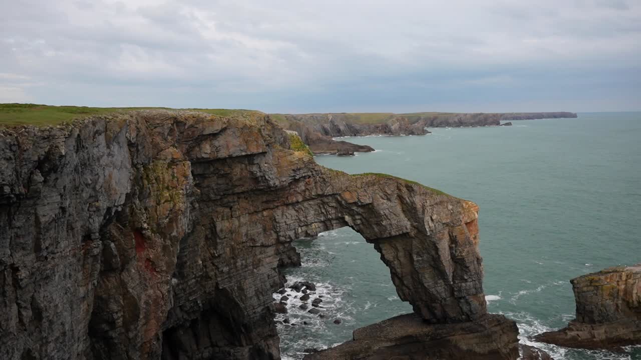 arco natural de piedra caliza en la costa de pembrokeshire, acantilados y cielos nublados