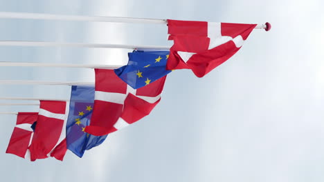 flags of denmark and european union hoisted on windy and cloudy day