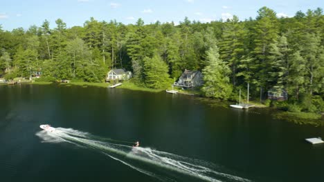 aerial drone following shot over a motor boat pulling a water skier on a bright sunny day in sunset lake in new hampshire, usa