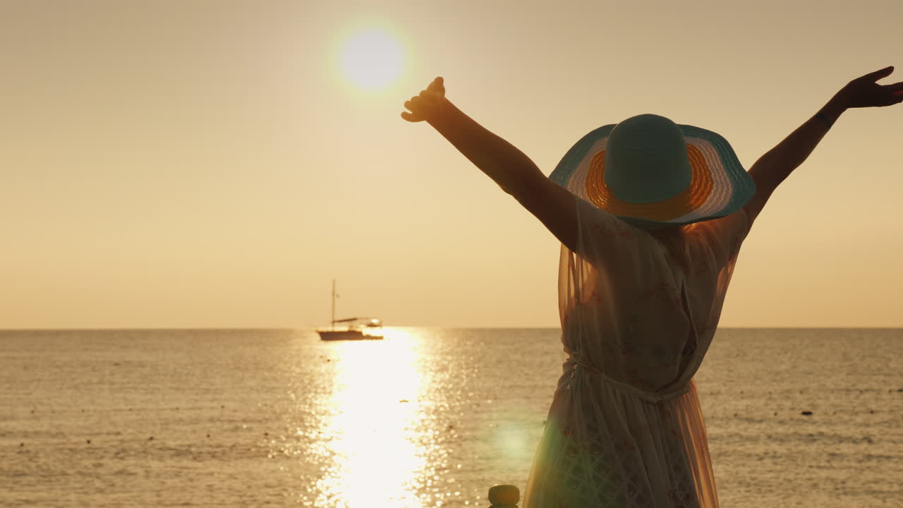 una mujer joven disfruta del amanecer sobre el mar agitando emocionalmente sus manos un barco es visible en el