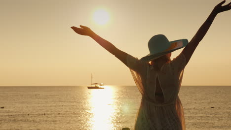 una mujer joven disfruta del amanecer sobre el mar agitando emocionalmente sus manos un barco es visible en el