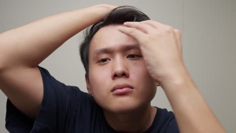 젊은 잘생긴 아시아 남자의 초상화. 손으로 검은 머리카락을 만지고, 얼굴을 바라보고.
