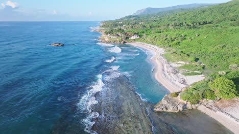 Drone-overview-showing-waves-of-Caribbean-sea-reaching-sandy-beach-and-green-coastline-of-Barahona