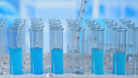 Scientist-injecting-chemicals-into-test-tubes.-Test-tube-of-colored-liquid-on-the-lab-table-in-the-background-of-the-glass-flasks.-poured-from-glass-pipette-into-test-tube-illuminated-with-blue-light.-High-quality-4k-footage