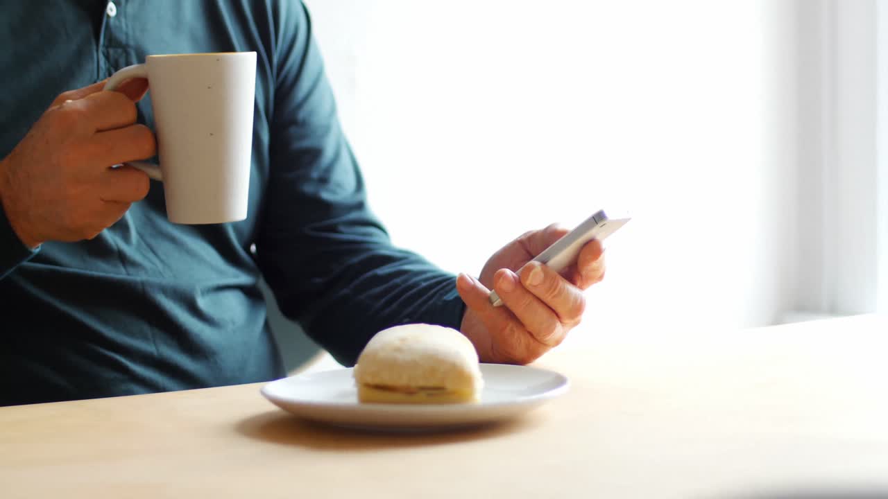 Man using mobile phone while having cup of coffee at home 4k