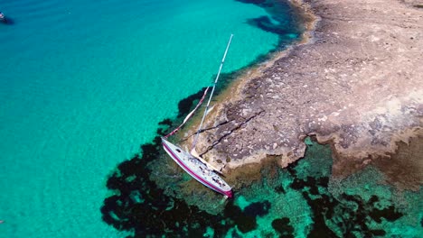 sailboat stranded on cliff near the coast of formentera island, spain, during a summer sunny day. spectacular aerial view flight drone camera pointing down