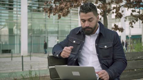 hombre enfocado pensando y trabajando con computadora portátil al aire libre
