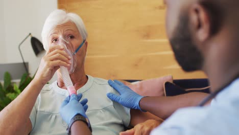 video of african american male doctor keeping oxygen to caucasian senior woman